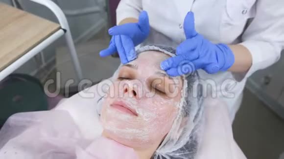 美容师将面膜卷在女人面部按摩动作上美容师面部治疗视频的预览图