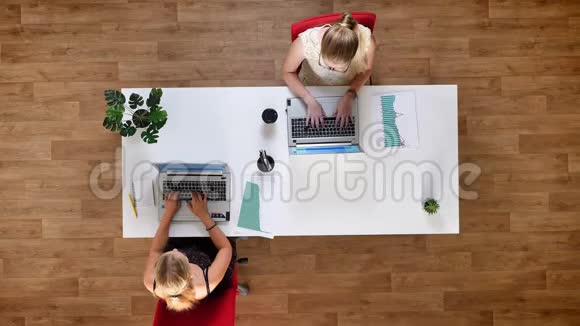 最下面的镜头两位辛勤工作的女性在笔记本电脑上打字坐在木制工作室的桌子旁视频的预览图