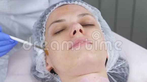 美容师用刷子把面具戴在女人脸上戴着蓝色橡胶手套的美容师的手面部视频的预览图