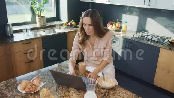 快乐的女人在厨房看视频微笑的女性看电脑视频的预览图