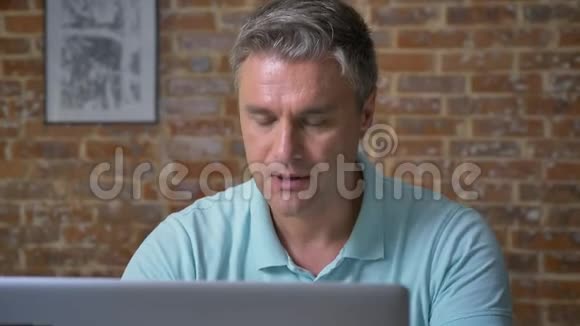 特写镜头集中的白种人成年商人正在电脑上打字而坐在办公室设计的砖块上与世隔绝视频的预览图