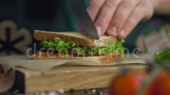 男人用锋利的刀在厨房的木板上把俱乐部三明治切成两半在家里做快餐厨师视频的预览图