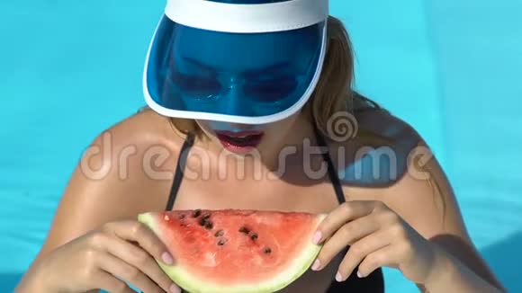 在游泳池里吃西瓜片的时髦女人微笑着吃零食视频的预览图