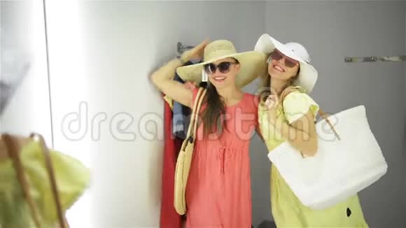 两个女人在镜子附近购物尝试滑稽的衣服适合客房的漂亮年轻购物者视频的预览图