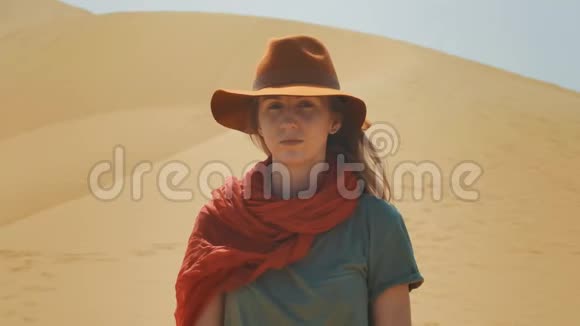 肖像沙漠中的女孩旅行者在沙滩上戴着帽子和红领巾探索古老的地形寻找视频的预览图