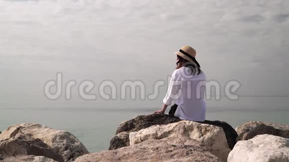 坐在岩石上看大海的女人的后景视频的预览图