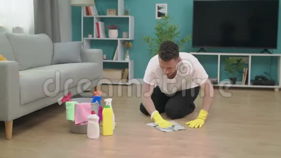 在家里打扫完卫生后男人坐在客厅的木地板上感到疲倦视频的预览图