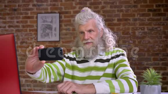 一位留着大白胡子的老白种人正坐在一间砖房里额头布满皱纹的自拍视频的预览图
