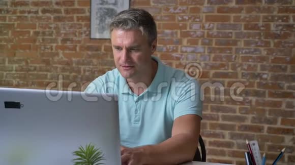 一个成熟的白人商人在他的笔记本电脑上打字后用拳头展示他的胜利姿态视频的预览图
