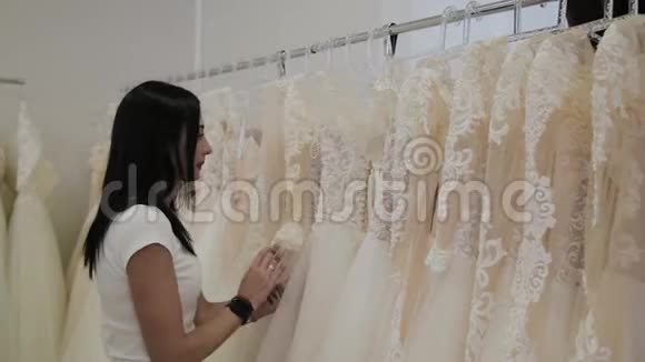 美丽的女孩在婚礼沙龙里选择婚纱男人躲在礼服里视频的预览图
