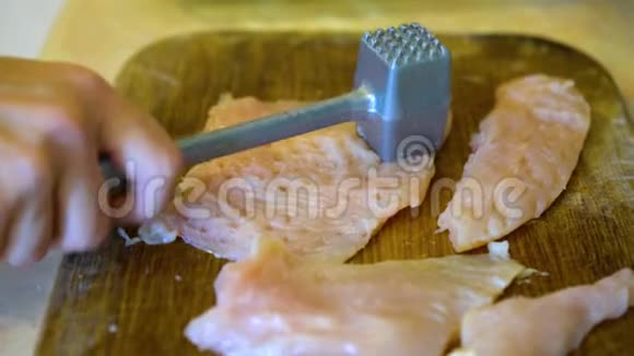 在家厨房的木制厨房板上女人用肉锤在桌上敲打着新鲜的生肉生菜视频的预览图