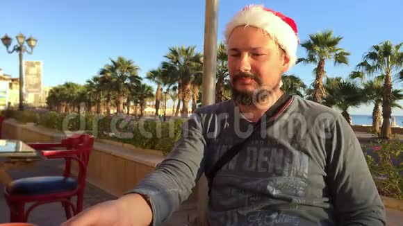 戴着圣诞帽的大胡子在喝咖啡棕榈树和海洋环绕视频的预览图