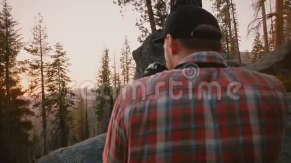 后景年轻男性摄影师拍摄美丽的森林日落照片在约塞米蒂山公园岩石缓慢运动视频的预览图