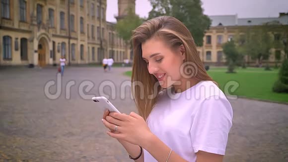 令人敬畏的白种人女孩正在滚动她的手机同时站在街上的个人资料寒冷和专注的傻笑视频的预览图