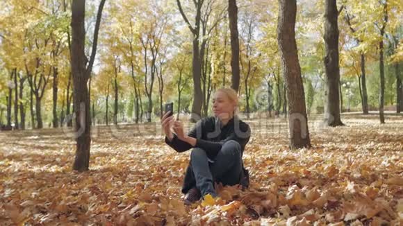 秋天的城市公园里一个女人坐在黄色落叶上自拍视频的预览图