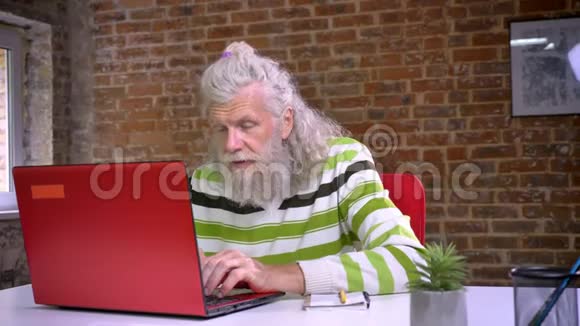 漂亮的白种人爷爷坐在红砖房里用红色电脑和伸展身体来放松视频的预览图