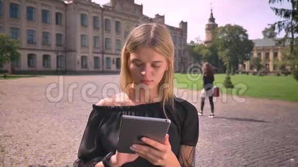 漂亮的白种人短发金发美女正在使用她的平板电脑并站在阳光的城市街道上视频的预览图