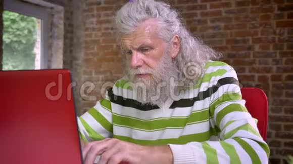 有趣的高白种人正在他的笔记本电脑打字坐在现代化的砖制办公室里他的脸视频的预览图
