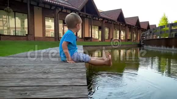 4k视频在欧洲的小运河里坐在河岸上双脚抱在水中笑容满面的孩子视频的预览图
