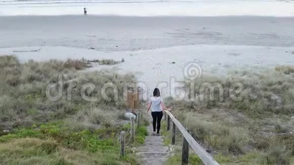 女孩欣赏日落景色在美丽的海滩前走下楼梯视频的预览图