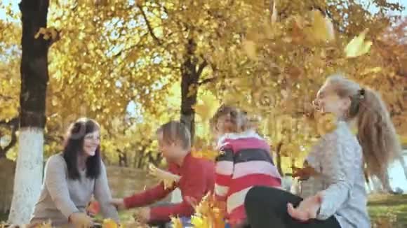 在阳光明媚的秋天天气里快乐的一家人在户外玩落叶父母在后台接吻视频的预览图