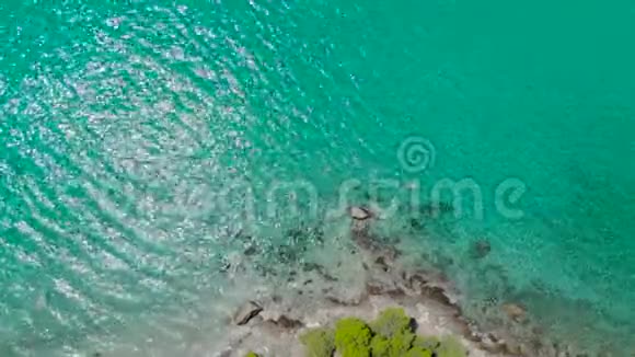 在岩石海岸的蓝色海面上用光线反射的鸟瞰透明绿松石海洋水面和r的俯视图视频的预览图