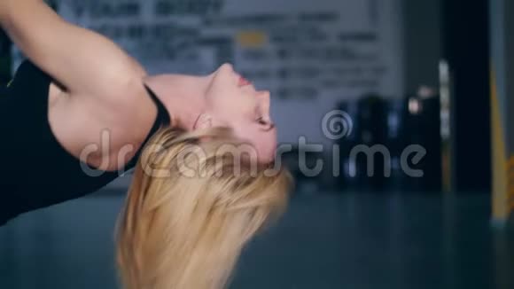 特写迷人的金发女人在黑色的顶部倒着流着的头发在TRX循环上进行练习陷阱视频的预览图