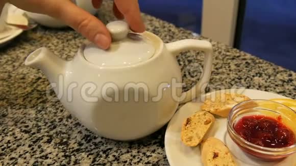 女人手抬起白色茶壶的盖子茶具瓷白茶壶和茶碟旁边有饼干柠檬视频的预览图