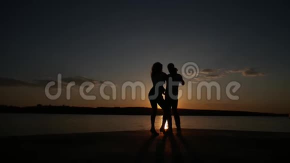 小男孩和小女孩在湖边日落时跳舞剪影拍摄视频的预览图