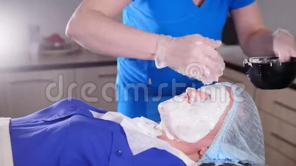 美容诊所年轻女子得到美容抗衰老治疗涂抹液体干燥面膜视频的预览图