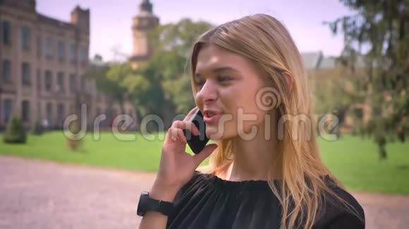 美丽的金发白种人女孩站着一边打电话一边风轻轻地移动她的头发城市景色视频的预览图