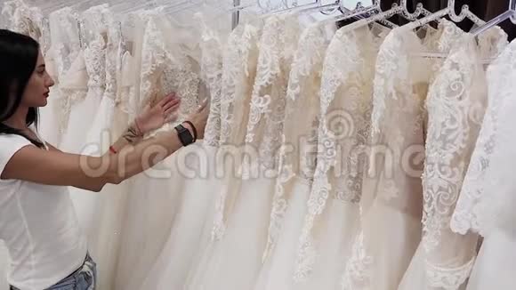 美丽的女孩在婚礼沙龙里选择婚纱男人躲在礼服里视频的预览图
