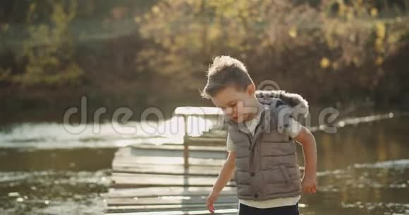 一个非常有魅力的三岁男孩站在湖边的桥上直视着他的画像视频的预览图
