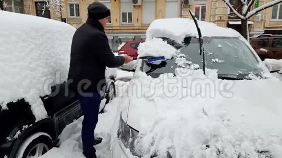 一名年轻人用伸缩刷子从暴风雪后的雪中清洁汽车的4K镜头视频的预览图