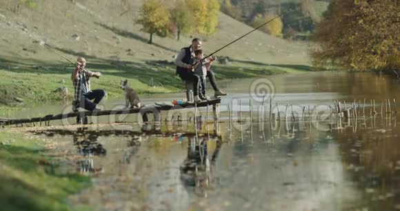 两个朋友在山中央的一个小湖里钓鱼一个可爱的小男孩站在爸爸的身边一个可爱的小男孩视频的预览图