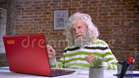 滑稽的白种人老爷爷留着长长的白胡子和头发坐在椅子上高兴地跳舞看着视频的预览图