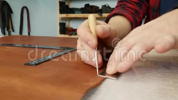 年轻的工匠用尺子和锥子在皮布上做一行标记手工皮革制品视频的预览图