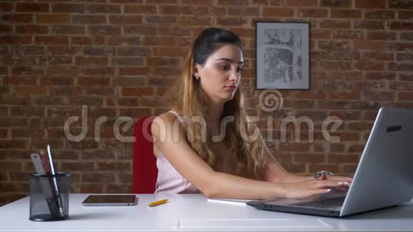 白种人漂亮的意图是在笔记本电脑上打字并在两者之间滑动她的平板电脑非常有效坐在她身边视频的预览图