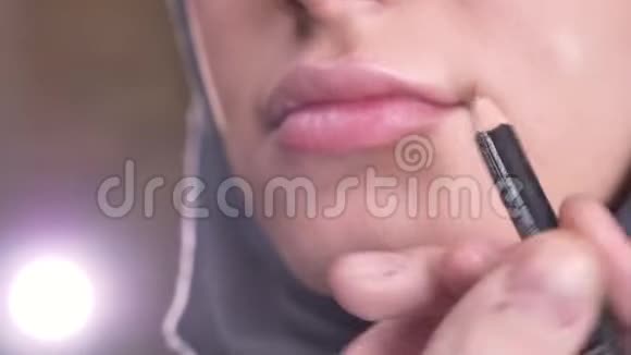 在黑色背景的穆斯林少女头巾上做化妆和涂粉红色口红的过程的特写镜头视频的预览图