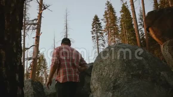 镜头跟随年轻的当地男子徒步旅行爬上大森林石头观看史诗般的日落在约塞米蒂慢动作视频的预览图