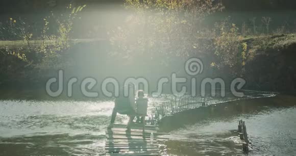 难忘的时刻爸爸和他的小儿子在湖边钓鱼坐在桥上的椅子上视频的预览图