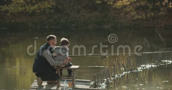 爸爸鼓励儿子钓鱼他们在晴天坐在桥上在红色的Eepic上射击视频的预览图