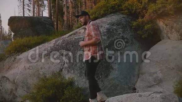 后景年轻的男性摄影师站在岩石上拍摄美丽的日落约塞米蒂公园森林慢动作视频的预览图