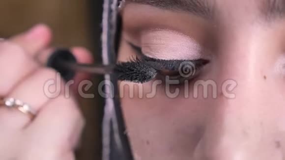 在明亮的灯光下用睫毛膏为戴着头巾的穆斯林妇女做化妆的特写照片视频的预览图