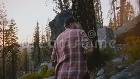 镜头跟随年轻的自由男子徒步旅行爬上大森林岩石在美丽的日落在约塞米蒂公园慢动作视频的预览图