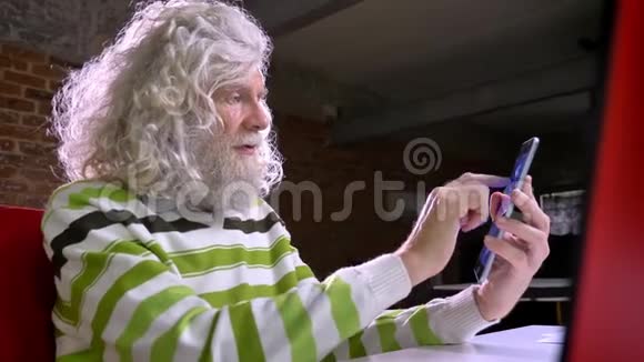 可爱的白种人奶奶留着漂亮的白胡子和头发在平板电脑上显示着蓝色的屏幕放松和平静砖块视频的预览图