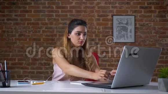 美丽的白种人女人坐在她的笔记本电脑旁边一边用耳机听音乐一边继续视频的预览图