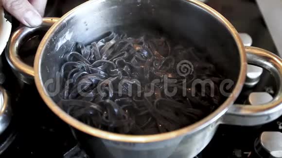 用勺子搅拌黑色意大利面在平底锅中加入墨鱼油墨乌贼油墨的硬粒小麦半果视频的预览图