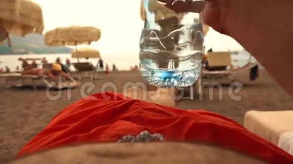 一名男子在海滩上用塑料瓶饮水的照片视频的预览图