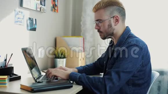 用眼镜和黄色头发特写年轻迷人男人的肖像在日记上做笔记家庭自由职业者视频的预览图